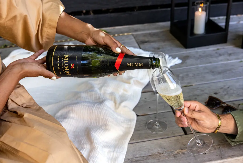 A person pouring Mumm Sparkling Brut Prestige into a sparkling wine glass